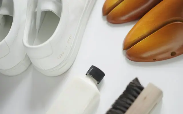 Sneakers albi lângă o perie și o soluție de curățat încălțăminte