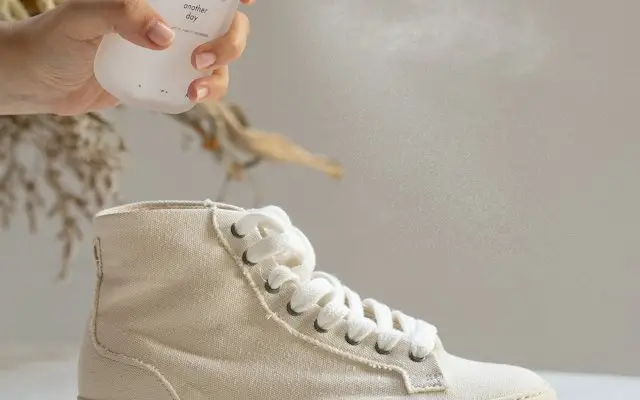 Persoană care pulverizează un spray de îngrijire pe un sneaker alb